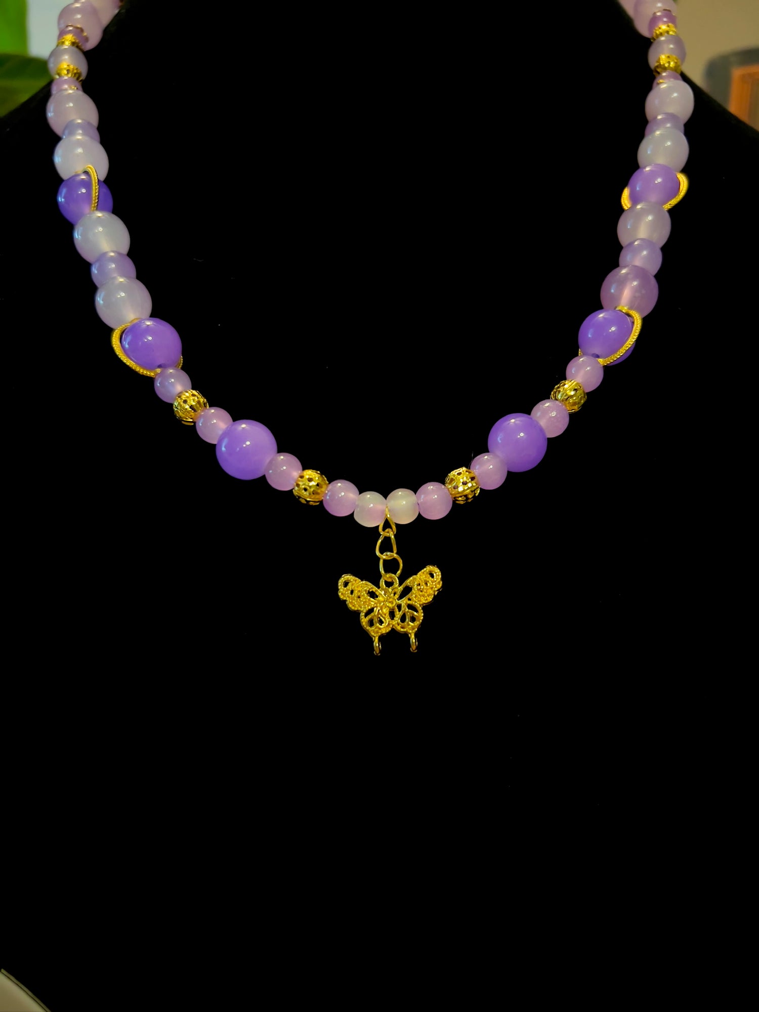 Necklace with purple beads and a gold butterfly charm on a black background